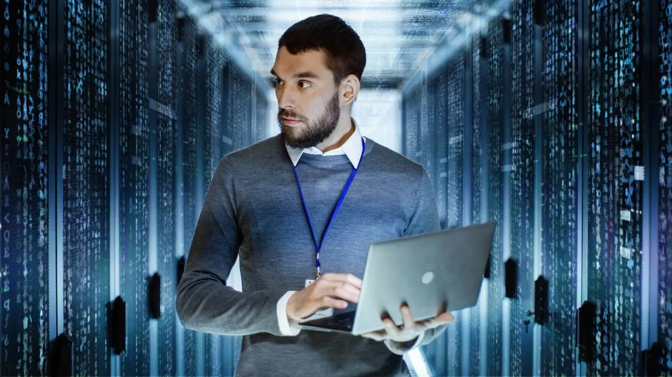 A man holding a laptop in front of some servers.